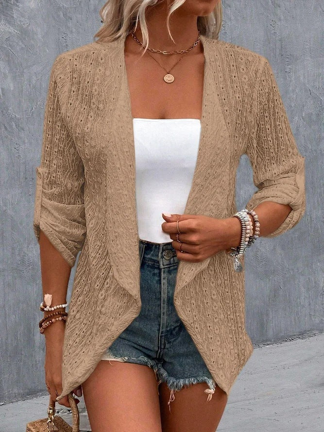 Femme portant un cardigan beige en tricot, débardeur blanc, short en jean, accessoires bracelets, collier doré, style décontracté chic.