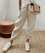 Pantalon en lin beige décontracté, porté avec un t-shirt blanc, des baskets blanches et un sac en osier, style mode estivale chic et confortable.