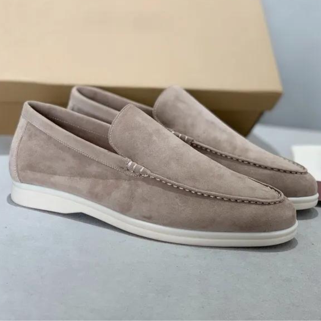 Paire de mocassins en daim beige pour homme, semelle blanche, design élégant et moderne, posée sur une surface grise avec boîte en arrière-plan.
