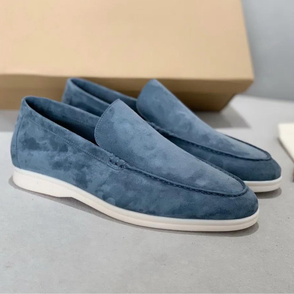 Mocassins en daim bleu pour homme, élégants et modernes, posés sur une surface grise avec boîte en arrière-plan. Chaussures tendance et confortables.