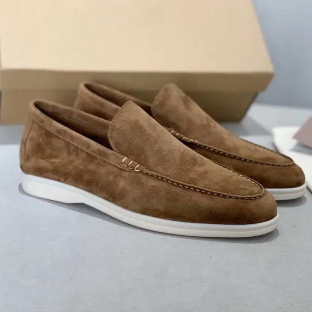 Mocassins en daim marron pour homme avec semelle blanche, posés devant une boîte en carton. Chaussures élégantes et confortables.