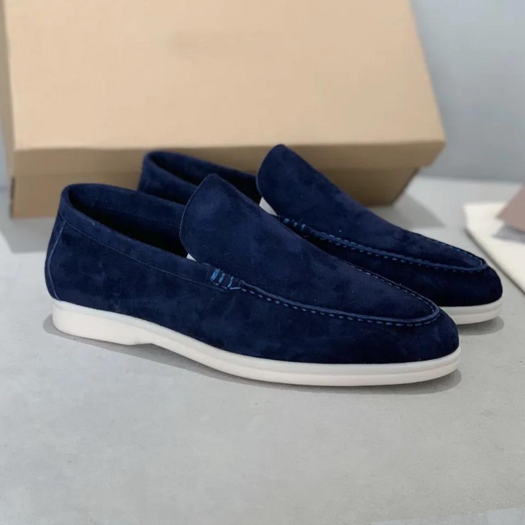 Mocassins en daim bleu marine pour homme, élégants et modernes, posés sur une surface grise avec boîte en arrière-plan. Chaussures tendance et confortables.