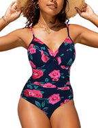 Femme portant un maillot de bain une pièce à fleurs roses sur fond bleu marine, style croisé, bretelles fines, accessoirisé d'un chapeau de paille.