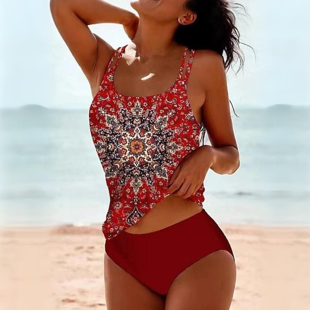 Femme en maillot de bain rouge à motifs mandala sur plage ensoleillée, souriante, mer en arrière-plan. Mode plage, été, vacances.