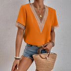 Femme portant un t-shirt orange à col en V avec dentelle, short en jean, et tenant un sac en osier. Mode estivale, tenue décontractée chic.