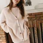 Femme portant un cardigan beige en maille devant une cheminée en briques. Mode automne, style décontracté, vêtements confortables.
