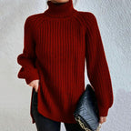 Femme portant un pull rouge à col roulé en tricot, tenant un sac à main noir matelassé avec chaîne dorée. Mode automne-hiver, style élégant.