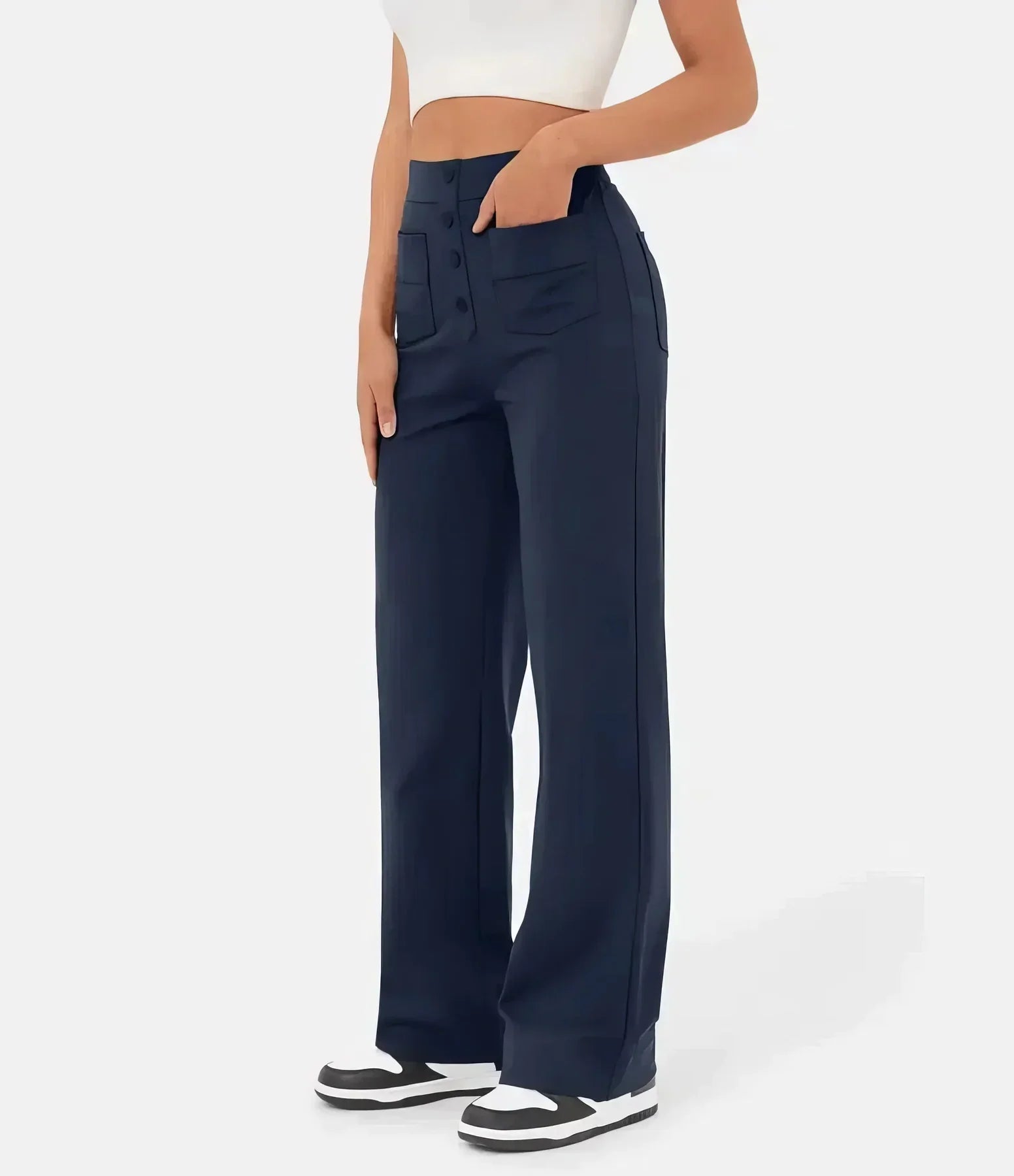 Femme portant un pantalon large bleu marine taille haute avec poches, associé à un haut blanc court et des baskets noires et blanches.