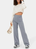Femme souriante portant un pull blanc et un pantalon large gris, tenant un sac beige. Mode décontractée, tendance automne, style urbain chic.