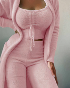 Femme portant un ensemble rose en tissu texturé, composé d'un haut à manches longues, d'un débardeur et d'un pantalon taille haute. Mode féminine élégante.