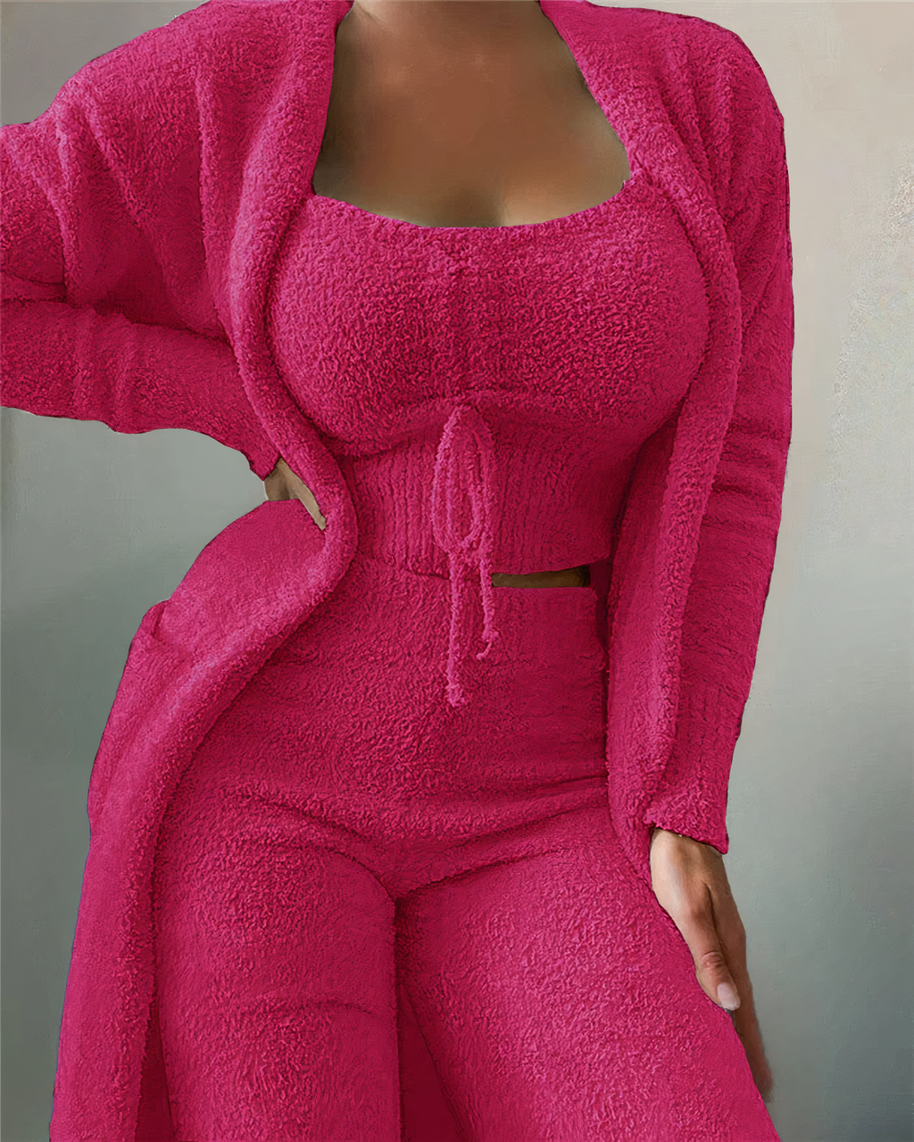 Femme portant un ensemble rose en tricot texturé, composé d'un cardigan, d'un haut court et d'un pantalon. Mode féminine, tenue confortable.