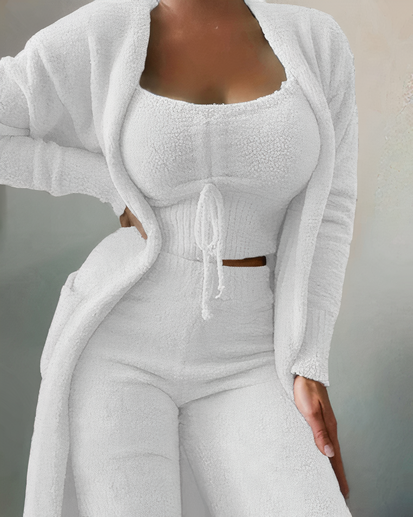Femme portant un ensemble loungewear blanc en tricot, composé d'un cardigan, d'un top court et d'un pantalon. Mode confortable et élégante.