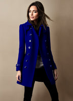 Femme portant un manteau bleu élégant, double boutonnage, sur fond beige. Mode automne-hiver, style chic et moderne.