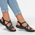 Sandales noires à brides croisées pour femme, portées avec un jean bleu clair. Chaussures d'été confortables et élégantes, semelle antidérapante.