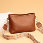 Sac à main en cuir marron avec bandoulière amovible à motifs géométriques, posé sur fond beige. Accessoire mode élégant et tendance.