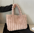 Sac à main en fausse fourrure beige avec anses texturées, posé sur un fond neutre. Accessoire mode tendance, élégant et doux au toucher.