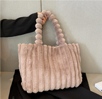 Sac à main en fausse fourrure beige avec anses texturées, posé sur un fond neutre. Accessoire mode tendance, élégant et doux au toucher.
