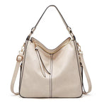 Sac à main en cuir beige élégant avec bandoulière réglable, fermetures éclair dorées et détails noirs. Accessoire mode femme chic et tendance.