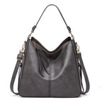 Sac à main en cuir gris élégant avec bandoulière amovible, fermeture éclair dorée, design moderne. Accessoire mode femme tendance et pratique.