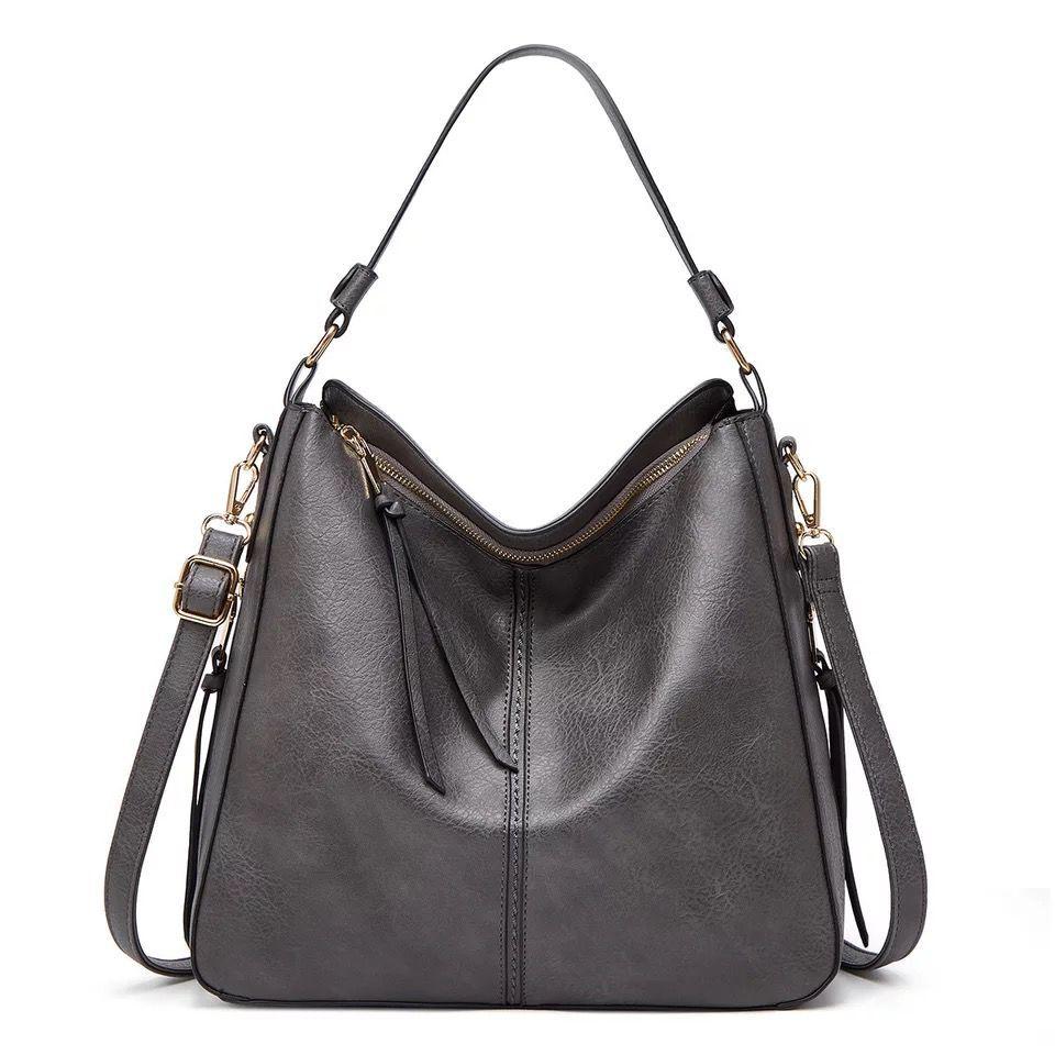 Sac à main en cuir gris élégant avec bandoulière amovible, fermeture éclair dorée, design moderne. Accessoire mode femme tendance et pratique.