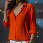 Femme portant une chemise orange vif, manches retroussées, avec un collier doré, sur fond flou. Mode féminine, style décontracté, élégance.
