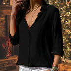 Femme en chemise noire élégante, devant un sapin de Noël illuminé, ambiance festive et chaleureuse, mode chic, soirée de fête.