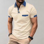Homme portant un polo beige à col bleu, manches courtes, poche poitrine, assorti à un pantalon beige. Mode masculine élégante et décontractée.
