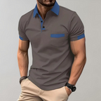 Homme portant un polo gris avec col bleu, manches courtes, poche poitrine, associé à un pantalon beige. Mode masculine élégante et décontractée.