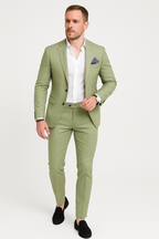 Homme en costume vert clair élégant, chemise blanche, pochette violette, montre-bracelet, chaussures noires. Mode masculine, style chic.