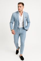 Homme en costume bleu clair, chemise blanche, pochette à motifs, chaussures noires. Mode masculine élégante, tenue formelle moderne.