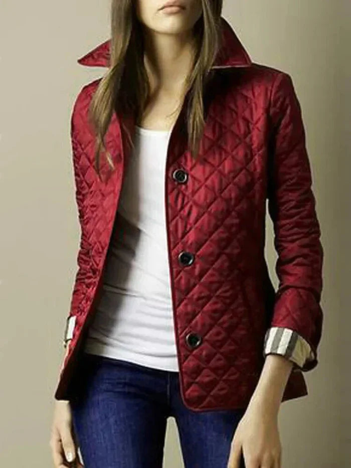 Femme portant une veste matelassée rouge élégante, col relevé, boutons noirs, manches retroussées, sur un t-shirt blanc et un jean bleu.