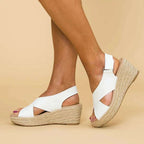 Sandales compensées blanches en cuir, semelle en corde, portées sur fond beige. Chaussures d'été élégantes pour femmes, confortables et tendance.