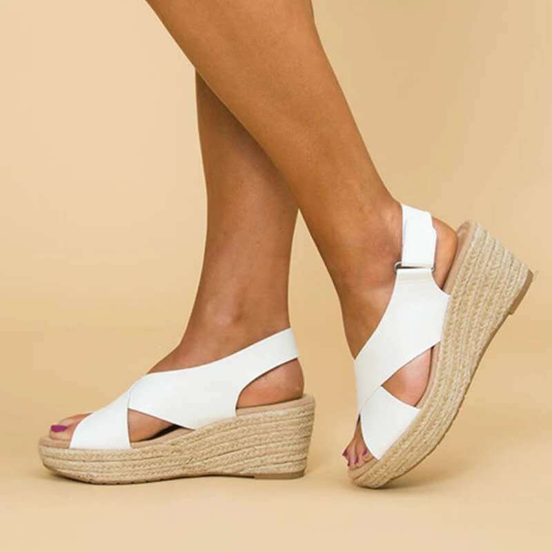 Sandales compensées blanches en cuir, semelle en corde, portées sur fond beige. Chaussures d'été élégantes pour femmes, confortables et tendance.