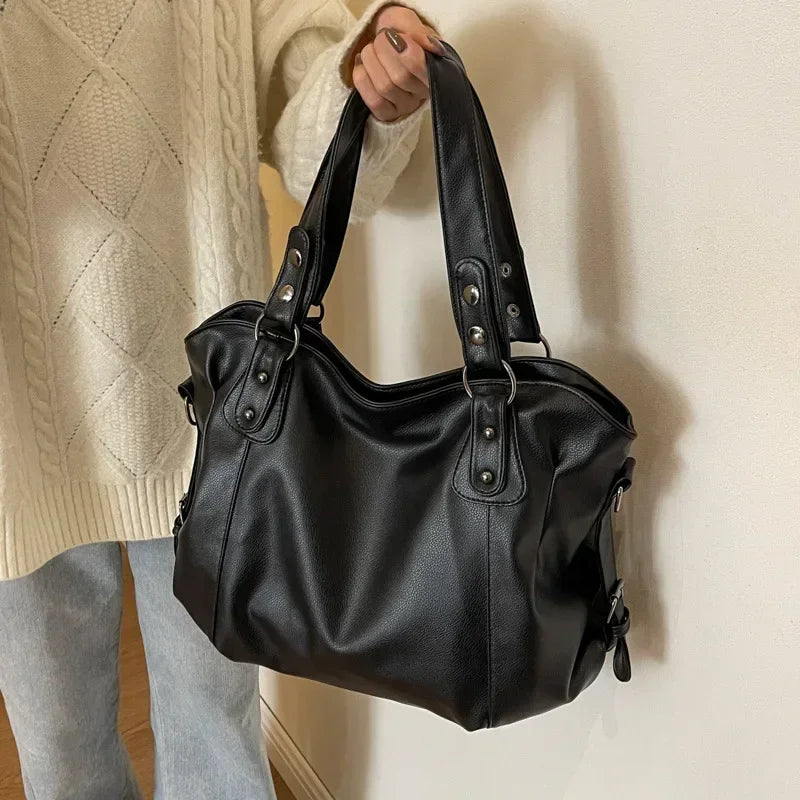 Sac à main noir en cuir porté par une personne en pull tricoté beige et jean. Élégant, moderne, idéal pour la mode automne-hiver.