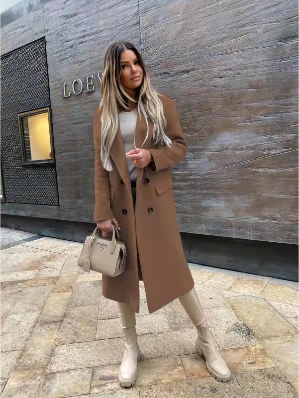 Femme en manteau marron, bottes beiges, tenant un sac à main Prada beige devant un mur moderne. Mode automne, style urbain chic.