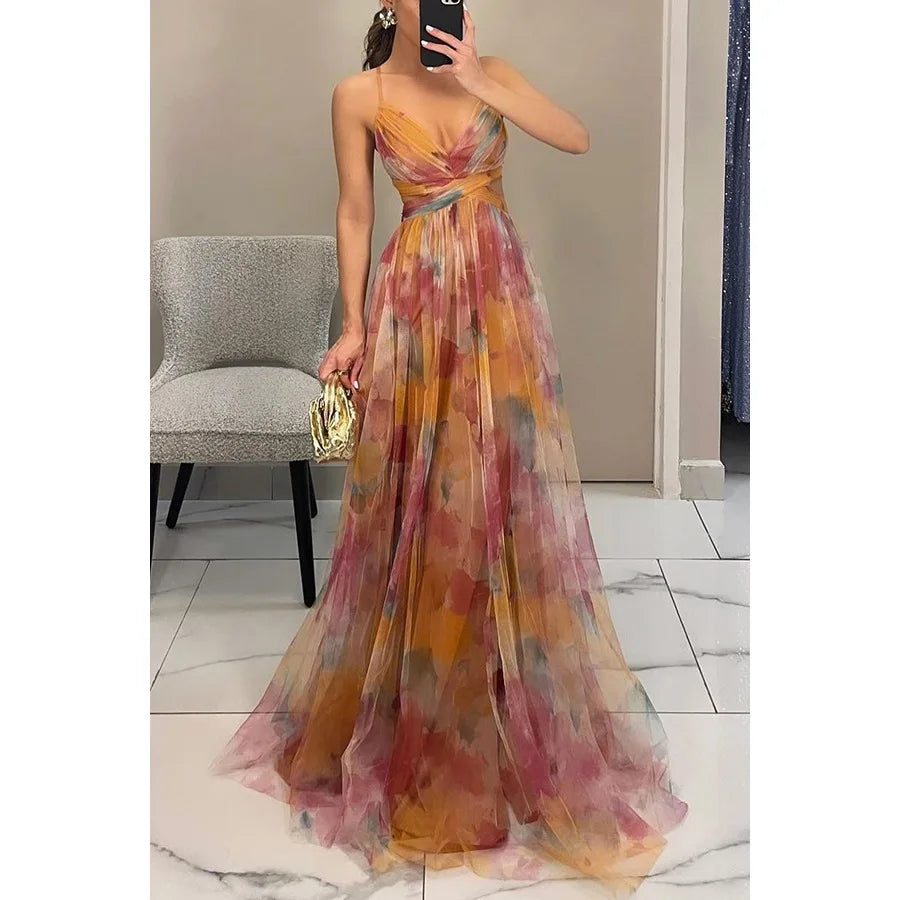 Robe de soirée longue multicolore, sans manches, avec motifs floraux, portée par une femme tenant un sac doré, sur fond de sol en marbre.
