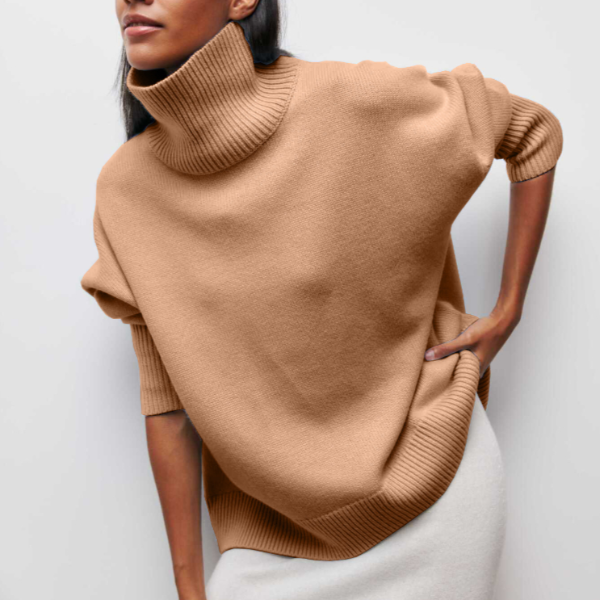 Femme portant un pull col roulé beige oversize, manches retroussées, sur une jupe blanche. Mode automne-hiver, style décontracté et élégant.