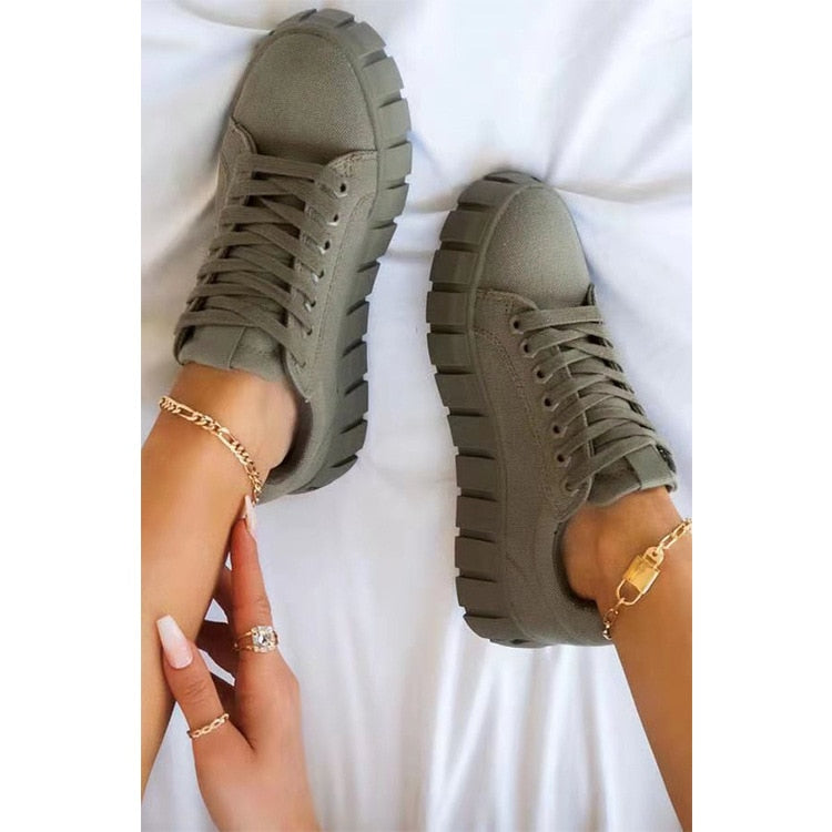 Chaussures de sport vertes avec semelles épaisses, portées par une personne avec des bracelets dorés sur les chevilles, posées sur un fond blanc.