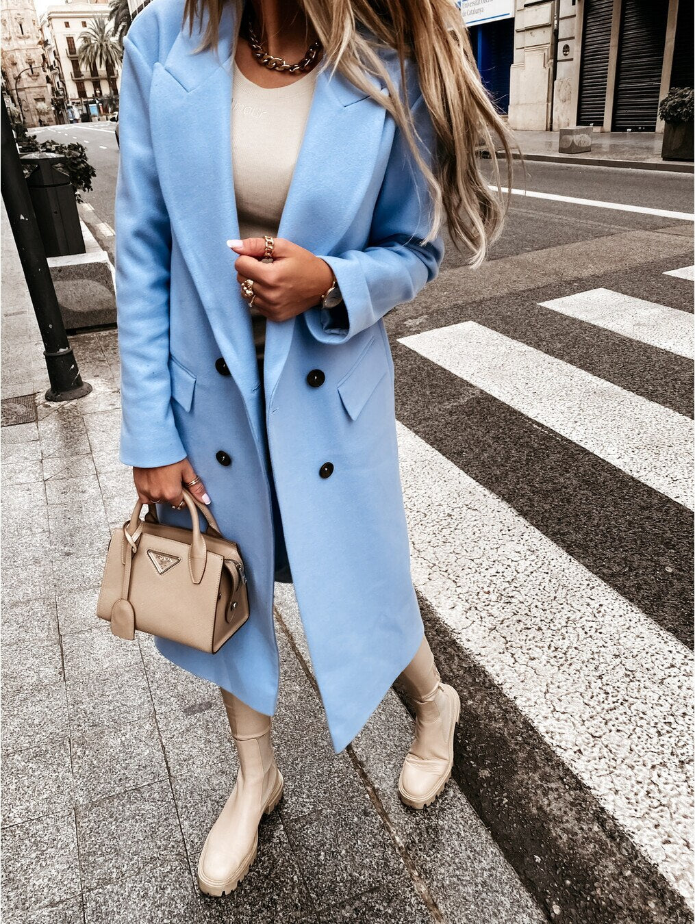 Femme en manteau bleu, sac à main beige Prada, bottes assorties, marchant en ville. Mode élégante, tendance automne, style urbain chic.