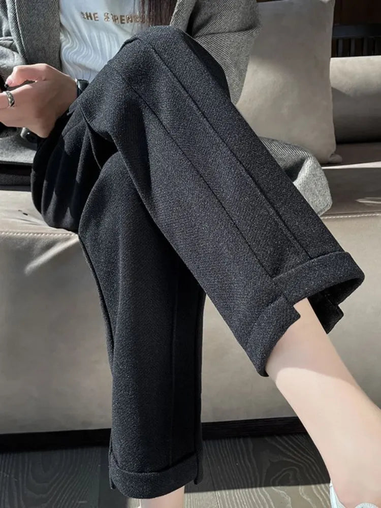 Pantalon noir élégant pour femme, coupe droite, tissu texturé, style décontracté chic, assise sur canapé beige, mode automne-hiver.