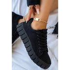 Chaussures noires tendance avec semelles épaisses, portées avec un bracelet de cheville doré. Mode féminine, baskets modernes, style urbain.