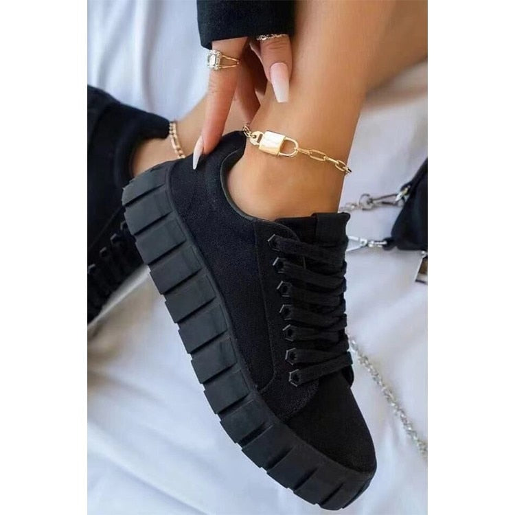 Chaussures noires tendance avec semelles épaisses, portées avec un bracelet de cheville doré. Mode féminine, baskets modernes, style urbain.