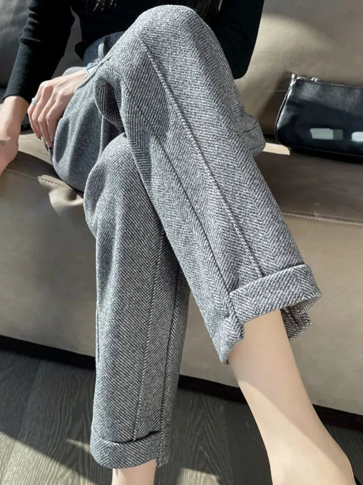 Pantalon en tweed gris pour femme, style décontracté, assise sur un canapé, sac à main noir à côté. Mode automne-hiver, tendance élégante.