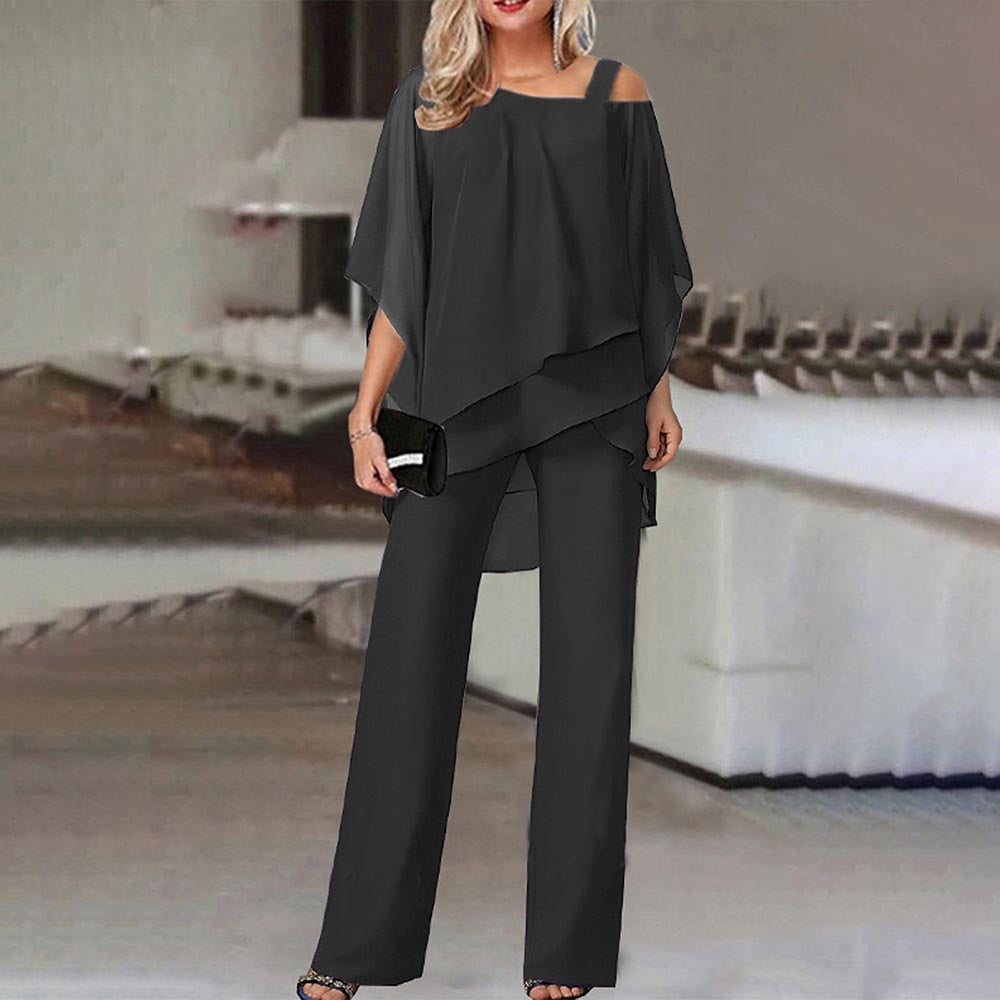 Femme en ensemble noir élégant, blouse asymétrique et pantalon large, tenant une pochette noire. Mode chic, tenue de soirée moderne.