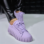 Chaussures baskets violettes tendance avec semelle épaisse, portées avec un pantalon en cuir noir. Mode urbaine, style moderne et élégant.