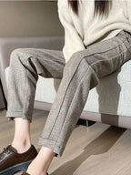 Pantalon en laine grise à chevrons, coupe droite, porté avec un pull beige et des chaussures marron, style automne-hiver élégant et décontracté.
