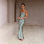 Femme en robe longue satinée verte dans un intérieur minimaliste, posant sur un sol en gravier. Mode élégante, style chic, tenue soirée.