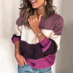 Femme souriante portant un pull tricolore violet, blanc et rose, manches retroussées, avec des bracelets dorés, posant décontractée.