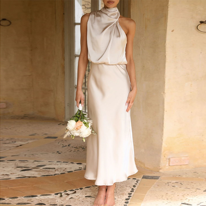 Robe de soirée en satin ivoire élégante, sans manches, avec col drapé, tenue par une femme tenant un bouquet de fleurs blanches, dans un cadre intérieur chic.