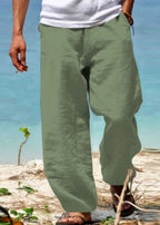 Pantalon ample vert kaki en lin pour homme, idéal pour l'été, porté sur une plage ensoleillée. Mode décontractée, confort, style estival.